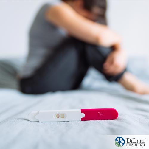 A woman in bed with a negative pregnancy test thinking of causes for infertility