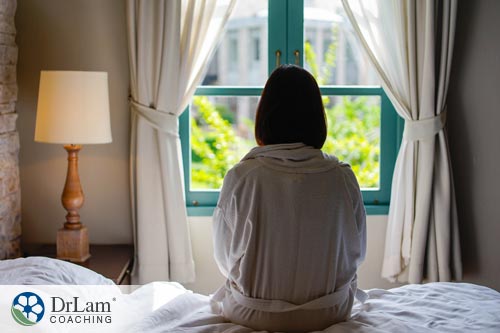 Young woman sitting on the edge of bed looking out into window thinking about pursuit of goals