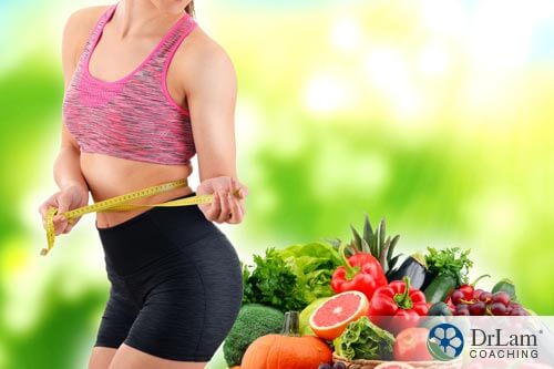 A woman holding a waist measuring tape around her waist and plant based diet next to her
