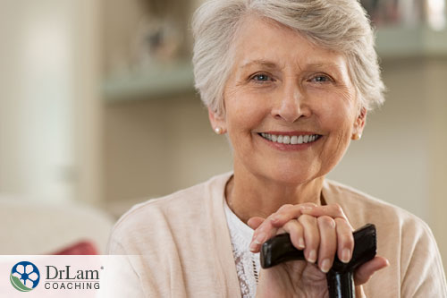 An image of an older woman smiling as she holds her cane