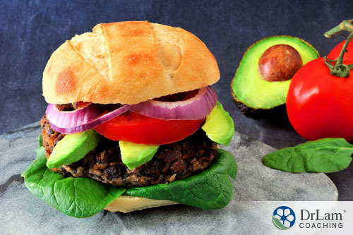 An image of a black bean burger on a whole grain bun with avocado, leafy greens, tomatoes and onions