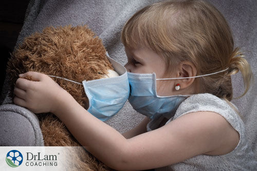 An image of a little girl and her teddy bear wearing protective masks