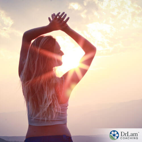 An image of a woman with her arms up in the sunshine staring off in the distance