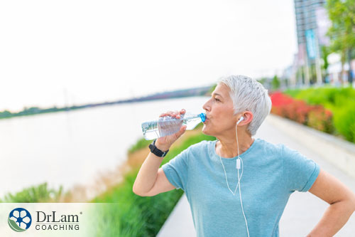 An image of an older woman drinking water while on a jog