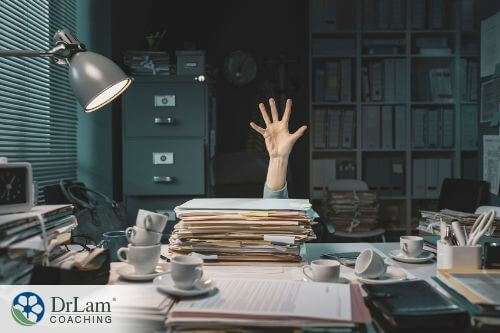 An image of a desk piled with papers and coffee cups and someone reaching out from behind them