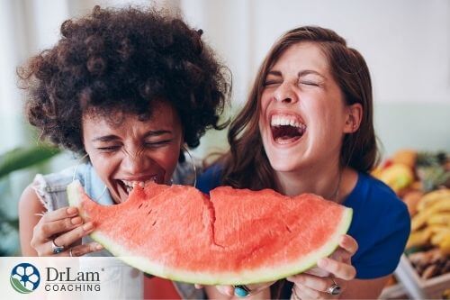 An image of two women laughing and eating watermelon