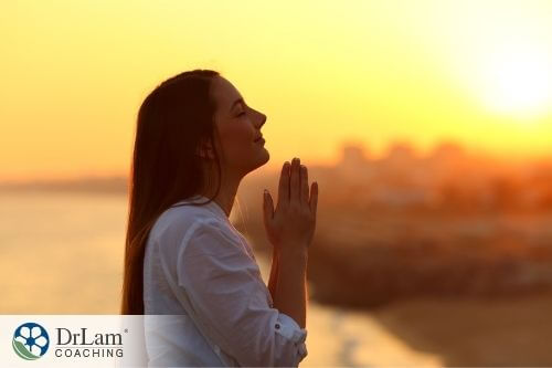 An image of a woman praying with the sun setting in the background