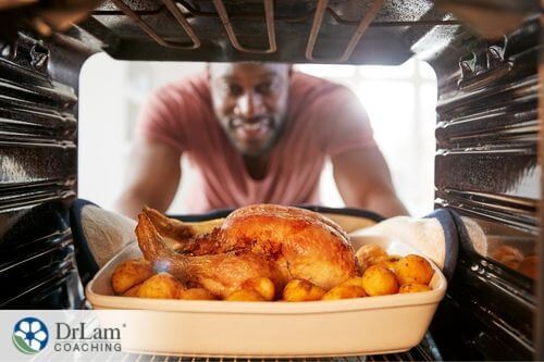 An image of a man pulling out a roasted chicken and potatoes from an oven