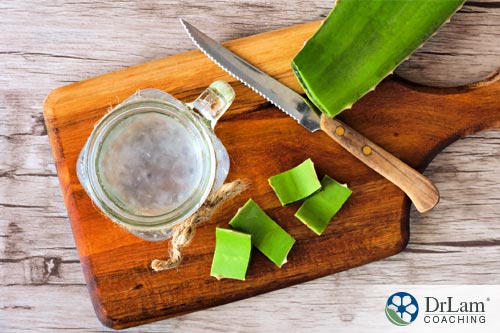 An image of some aloe vera being prepared on a wooden cutting board with a glass of aloe vera juice