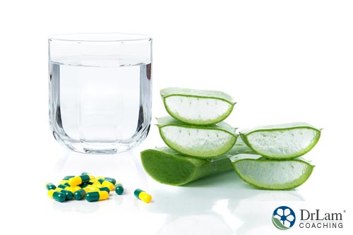 An image of a stack of sliced aloe vera next to some medications along with a glass of water