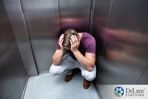 An image of a man squatting down in an elevator holding his head