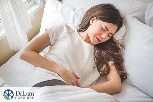 An image of a woman in bed holding her stomach in pain