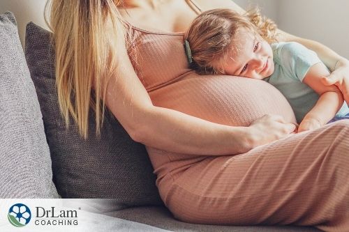 An image of a pregnant woman sitting on the couch with a kid hugging her belly