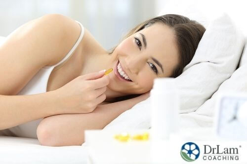 An image of a smiling woman laying in bed with a gel cap supplement in her hand