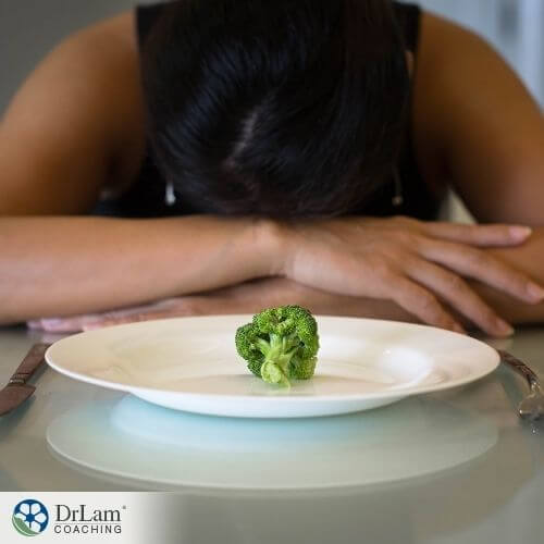 An image of a woman with her head down on the table an a broccoli on a plate