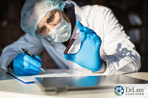 An image of a doctor wearing PPE holding and studying a vile of blood