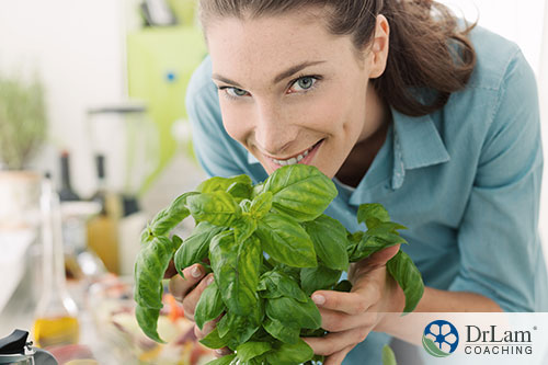 An image of a woman holding a basil plant close to her face smiling