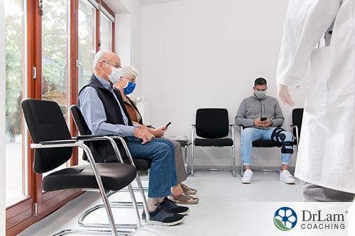 An image of an old couple sitting in the waiting room at a doctor's office wearing masks