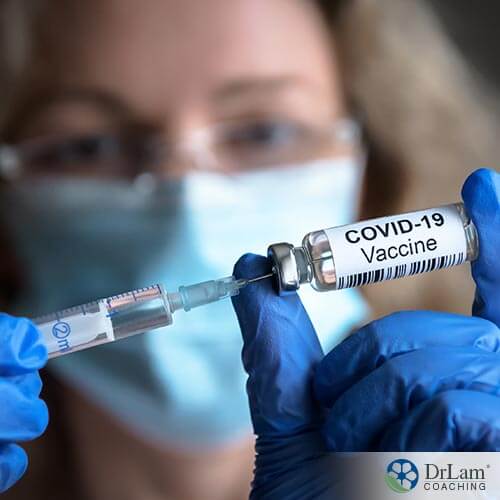 An image of a woman wearing a mask and gloves holding a vial of a COVID-19 Vaccine and needle