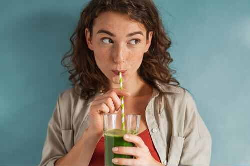 An image of a woman sipping a green drink