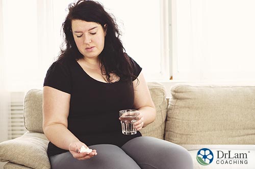An image of an overweight woman looking at a hand full of supplements