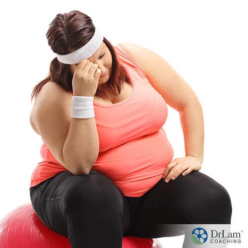 An image of an overweight woman sitting on an exercise ball looking discouraged