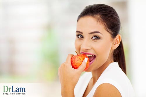 Young woman smiling and biting into an apple. A proper food combining diet will optimize nutrition from food eaten.