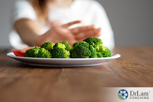 An image of a woman pushing away a plate of broccoli