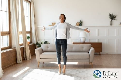 An image of a woman stretching her arms to the side while smiling in the living room