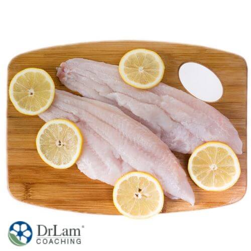 An image of white fish on a wood board topped with lemon slices