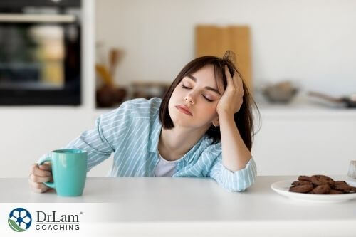 An image of a very fatigued woman leaning on a kitchen counter holding coffee