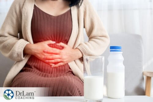 An image of a woman holding her stomach as she sits next to a glass of milk