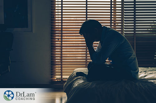 An image of a man sitting on his bed in a dark room holding his head