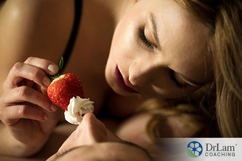 a woman holding a strawberry with cream on top giving to her partner intimitely