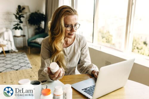 An image of a woman looking at her laptop as she holds a bottle of supplements