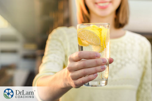 An image of a young woman offering a glass of lemon water