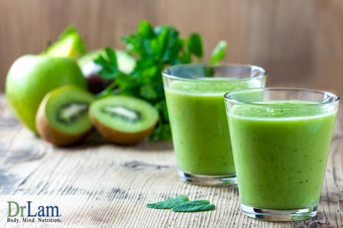 Two glasses of green smoothie with ingredients such as kiwi and apple in the background. A simple smoothie with just fruits, vegetables and water is best for the food combining diet.