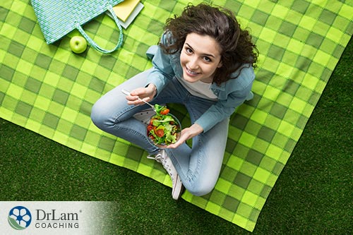 An image of a woman eating a green salad sitting on a green blanket outside