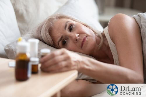 An image of an older woman laying in bed looking at her pill bottles