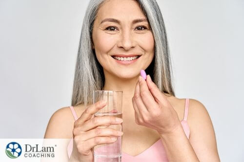 An image of a woman holding a pink pill and a glass of water