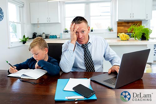 An image of a stressed out father trying to work while his son sits next to him doing schoolwork