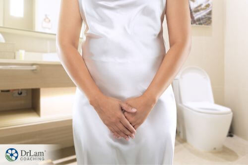 An image of a woman with her hands over her bladder while standing in the bathroom