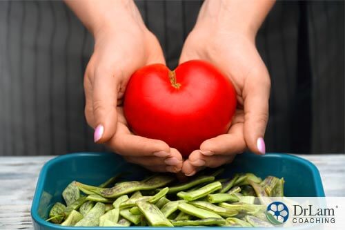 An image of hands holding a heart-shaped tomato over a bowl of green beans