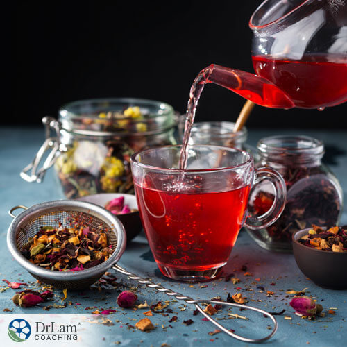 An image of red tea pouring into a clear glass mug with dried teas around it