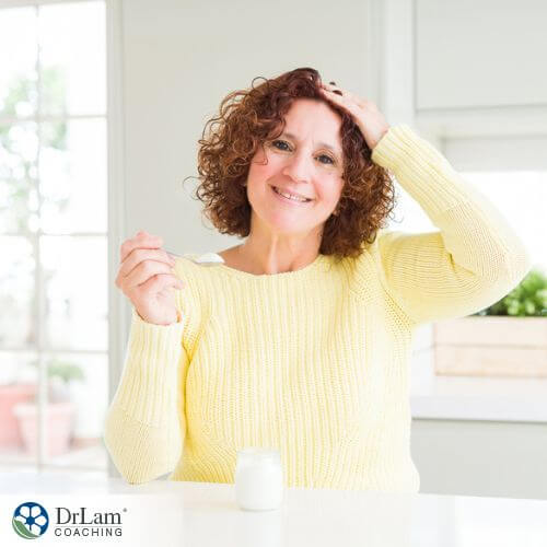 An image of a woman holding her head and eating yogurt