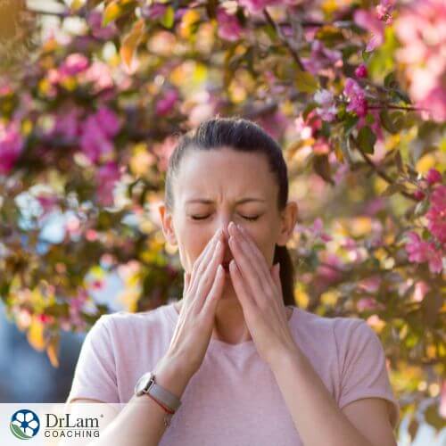 An image of a woman sneezing under a tree full of flowers