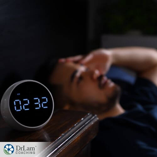 An image of a man trying to sleep with a clock showing the time is two thrity two in the morning