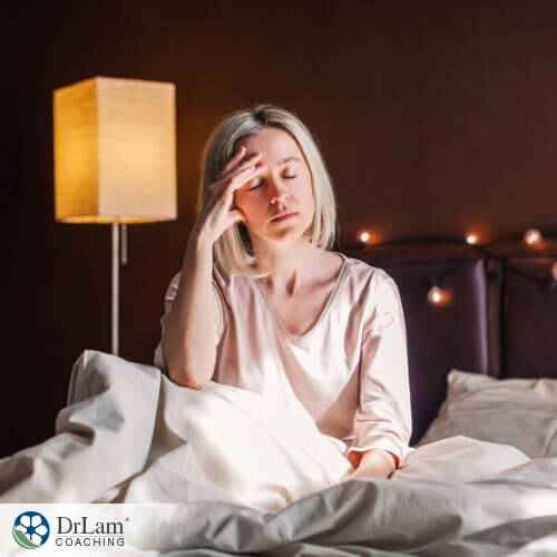 An image of a woman sitting on her bed with a headache