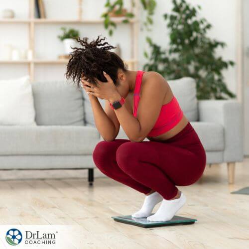 An image of a frustrated woman squatting on the scale holding her head