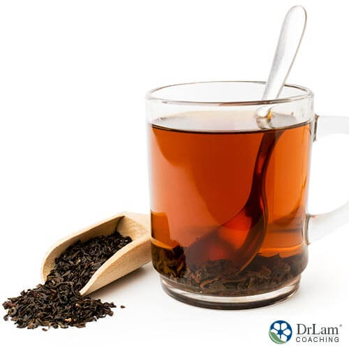 An image of a cup of black tea with a spoon and some black tea leaves